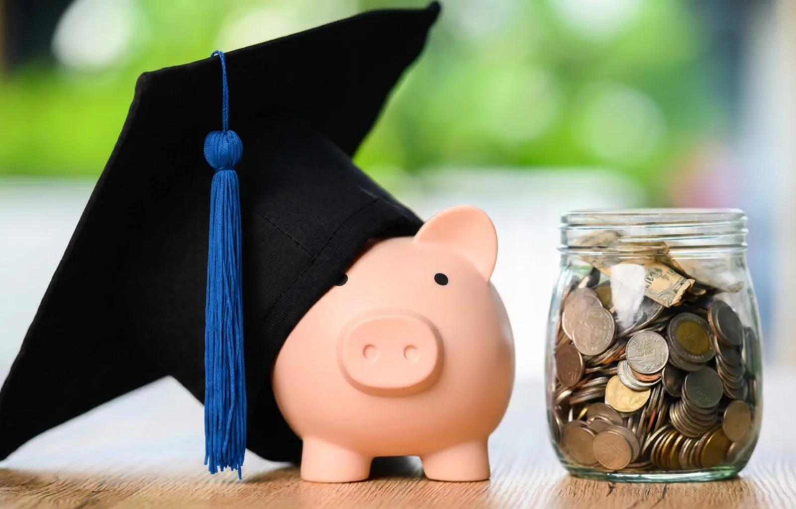 Piggy bank wearing a graduation cap beside a jar of coins, representing saving for education.